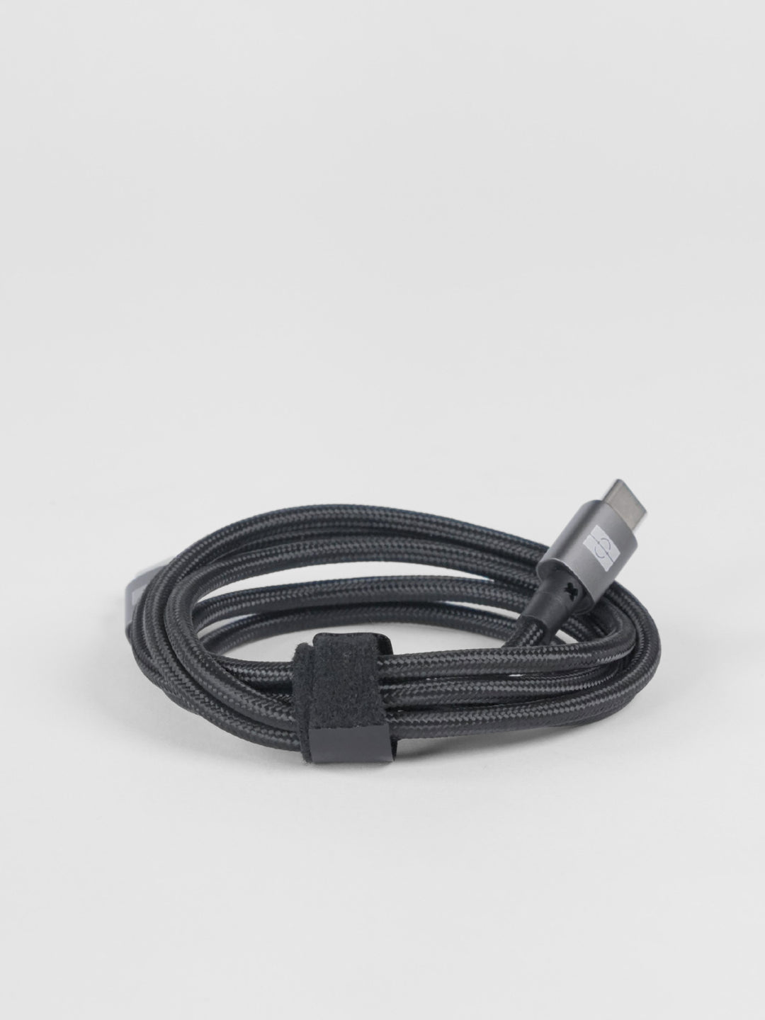 A neatly coiled dark gray braided Schlüssel USB-C charging and data cable with a premium dark gray metallic connector housing, secured by a black velcro strap on a light gray background